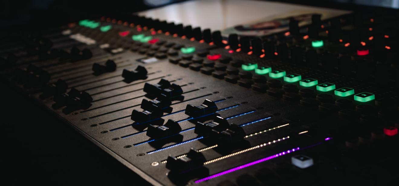 A close up of a soundboard shows colorfully backlit buttons and dials.