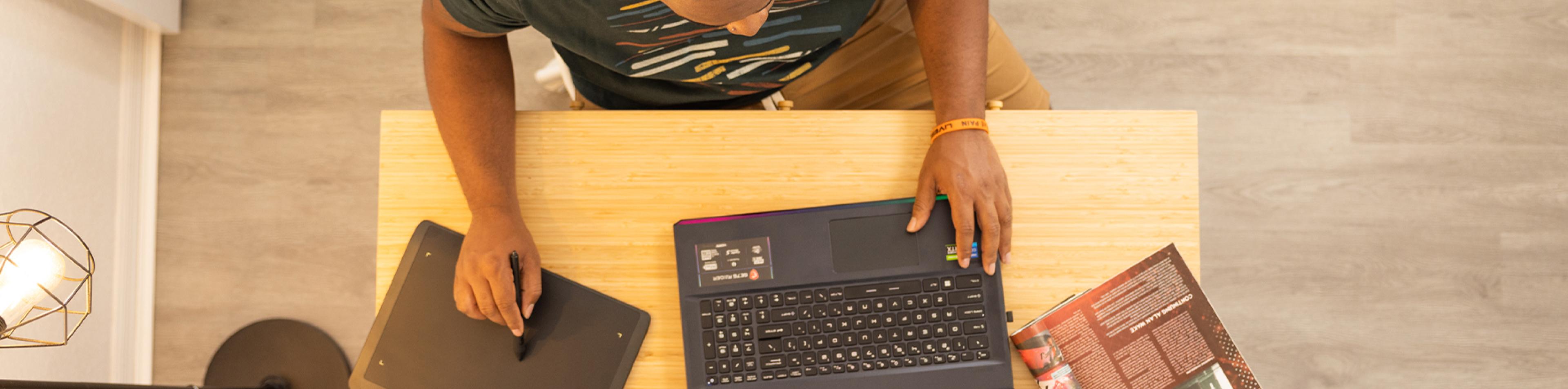 Overhead view of an Art & Design student using his pen tablet and laptop at a desk.