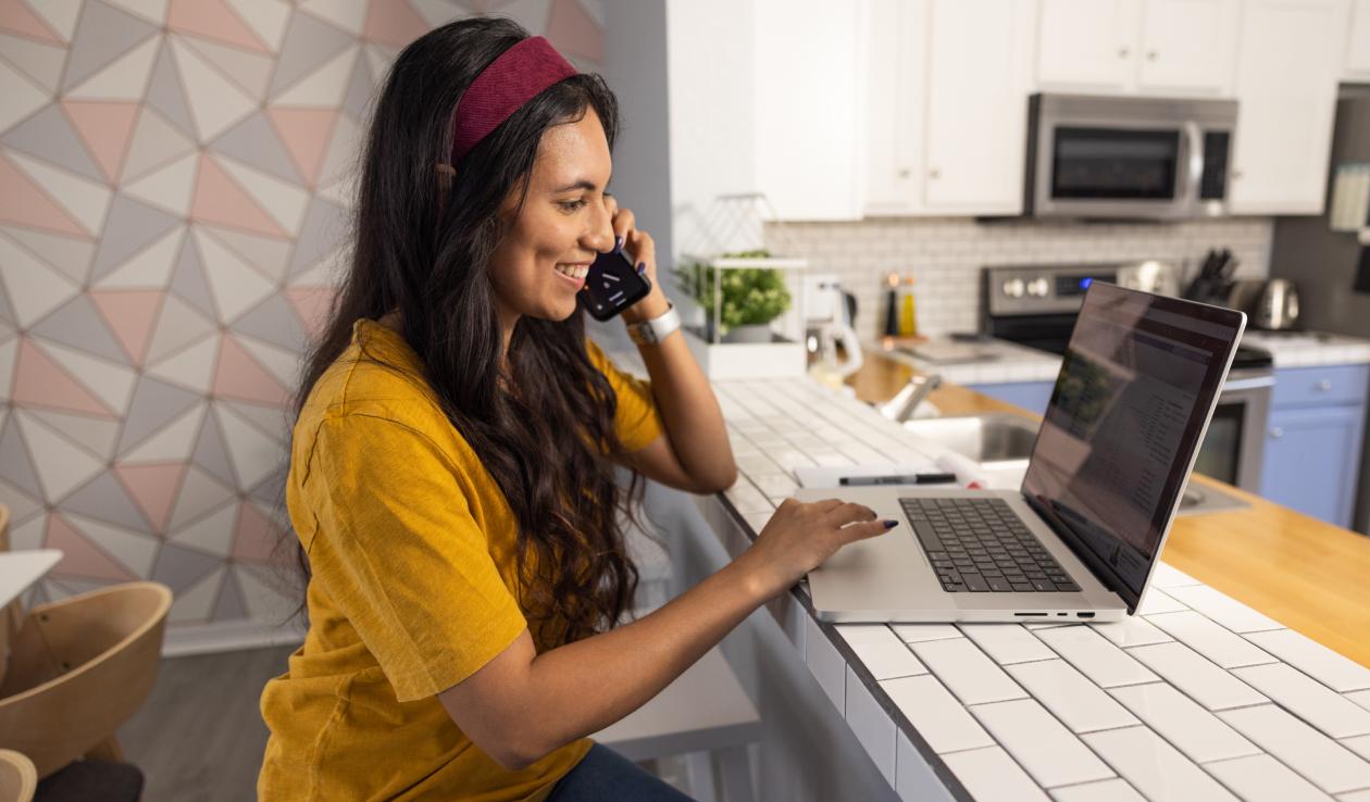 A female student takes a phone call while she works at her tiled kitchen counter.