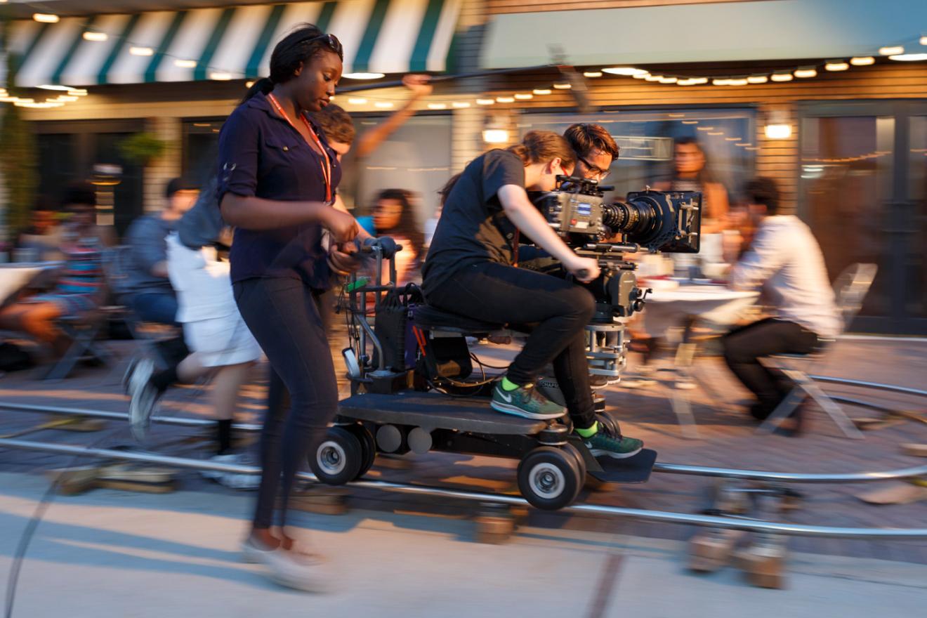 Students operate a camera on a dolly track while shooting an outdoor scene in the Full Sail Backlot.
