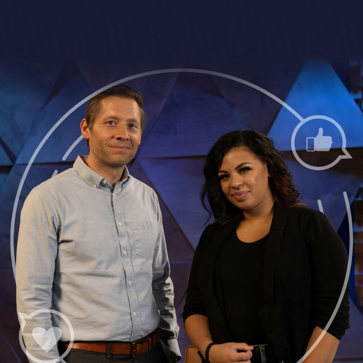 Tiffany Day and Sam Michie stand next to each other in front of a blue geometric background. Sam is wearing a light blue shirt and Tiffany is wearing a black t-shirt and a black blazer. They are both looking at the camera and smiling.