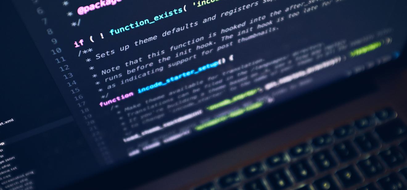 An up-close shot of a laptop shows colorful lines of code on a black screen.